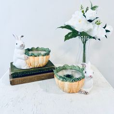 two ceramic rabbits sitting next to each other in front of a vase with white flowers