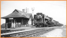 an old photo of a train coming down the tracks in front of a small station