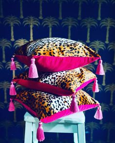 three pillows with pink tassels on them sitting on a stool in front of a blue wall