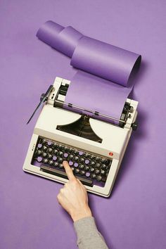 a person pointing at an old fashioned typewriter with purple paper on the top and bottom