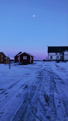 the road is covered in snow and there are two houses on either side of it