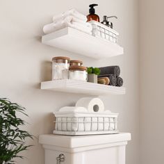 two white shelves above a toilet with towels and other items on top of the shelf