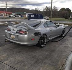 a silver sports car is parked at a gas station with its hood open and the fuel pump out