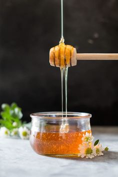 honey being poured into a glass jar with flowers on the side and a wooden stick sticking out of it