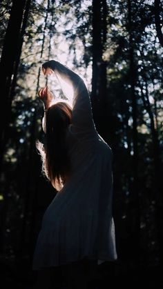 a woman standing in the woods holding her arms up to the sun's rays