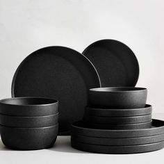 black plates and bowls stacked on top of each other in front of a white background