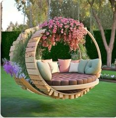 an outdoor swing chair with flowers hanging from the ceiling and pillows on the back, in front of a lush green lawn