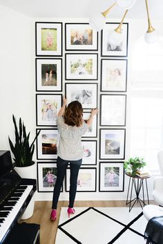 a woman standing in front of a wall with pictures on it and holding her hands up