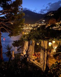 an outdoor area overlooking the water at night with lights on and people sitting in it