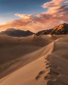 the sun is setting over sand dunes and mountains