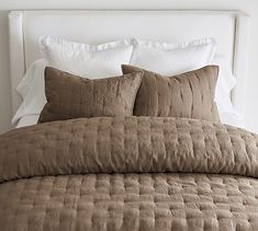 a bed with brown comforter and pillows in a white walled room next to a window