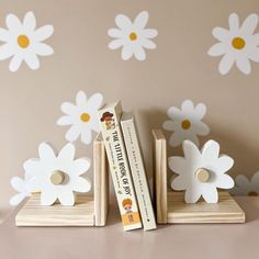 two books are stacked on top of each other with flowers painted on the wall behind them