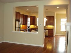 an empty living room and kitchen with hard wood flooring in the foreground, light from windows on the far wall