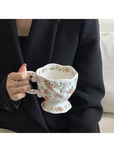 a woman in a black jacket holding a white coffee cup with pink flowers on it