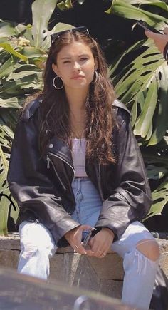 a young woman sitting on top of a cement wall next to palm trees and holding a cell phone