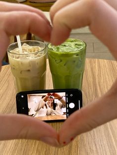 two people making a heart shape with their hands while taking a photo of some drinks