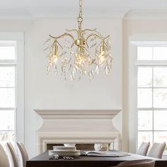 a chandelier hanging over a dining table in a room with white walls and windows