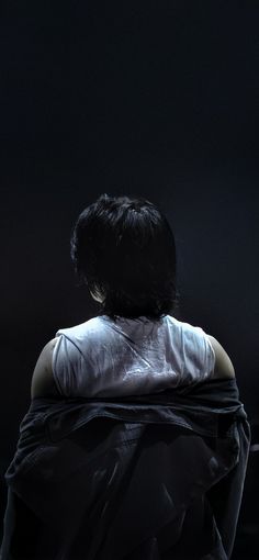 the back of a woman's head with black hair and white shirt over her shoulders