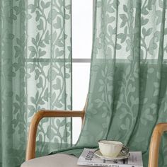 a chair with a cup sitting on top of it next to a window covered in green curtains