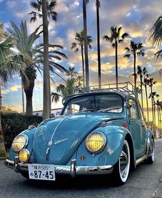 an old blue car parked on the side of the road with palm trees in the background