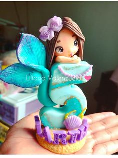 a little mermaid figurine sitting on top of a cupcake in someone's hand