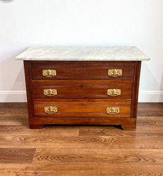 an antique chest of drawers with marble top and brass pulls on the bottom, against a white wall