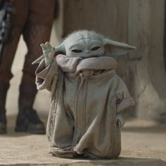 a baby yoda doll sitting on the ground with its hands up in front of it