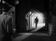 a man in a suit and hat walking into a dark room with light coming through the door