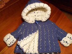 a crocheted blue and white coat sitting on top of a wooden table