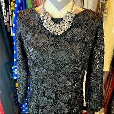 a mannequin wearing a black lace dress with an elaborate necklace on it's neck