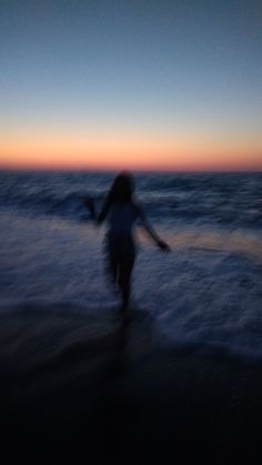 a woman is walking on the beach at sunset with her arms spread out and feet in the water