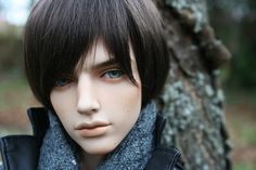 a mannequin head wearing a black jacket and gray scarf next to a tree