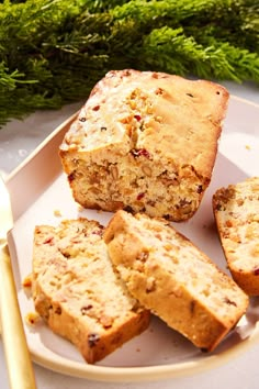 slices of fruitcake on a plate next to a knife and fork with some green plants in the background