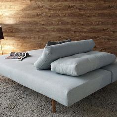 a gray couch sitting on top of a rug next to a lamp and wooden wall