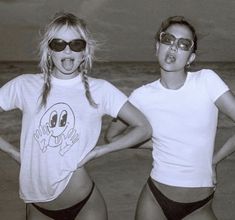 two young women standing next to each other on the beach