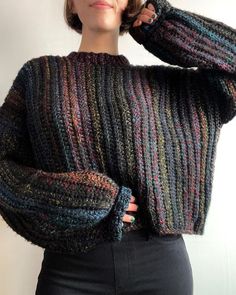 a woman wearing a multicolored sweater and black pants with her hands on her head