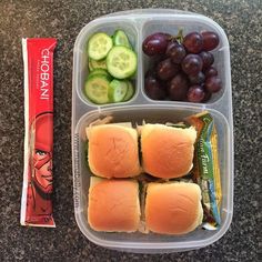 a plastic container filled with sandwiches and grapes next to a bag of chips on the counter