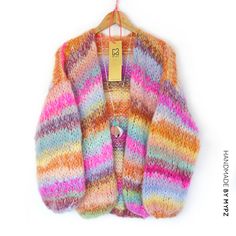 a multicolored cardigan hanging on a hanger with a tag attached to it