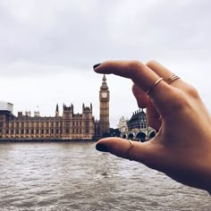 a person's hand holding out to the camera in front of a body of water