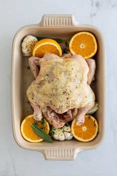 chicken with herbs and oranges in a casserole dish on a marble surface