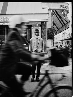 a black and white photo of a man standing in front of a store with his bicycle