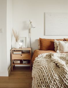 a bedroom with a bed, nightstand and pictures on the wall above it in white walls