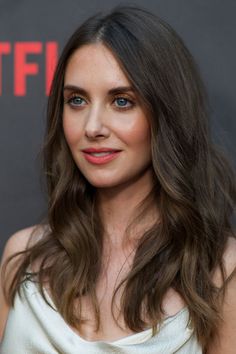 a woman with long brown hair and blue eyes posing for the camera in front of a red carpet