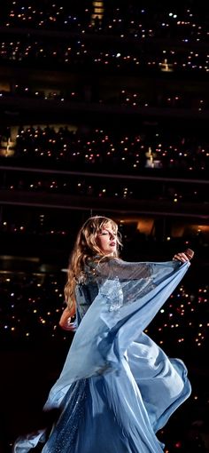 a woman in a blue dress standing on stage with her arms spread out to the side