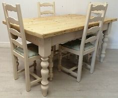 a wooden table with four chairs next to it on the floor in front of a white wall