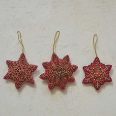 three red and gold ornaments hanging from strings on a white wall with no one around them