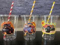 three plastic cups with monster trucks on them and two straws sticking out of the lids