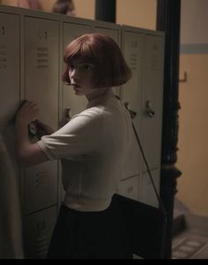 a woman with red hair standing in front of lockers