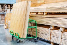 several stacks of wooden planks in a warehouse with a green hand truck full of them