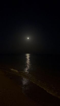 the moon shines brightly in the dark sky over the water on a beach at night